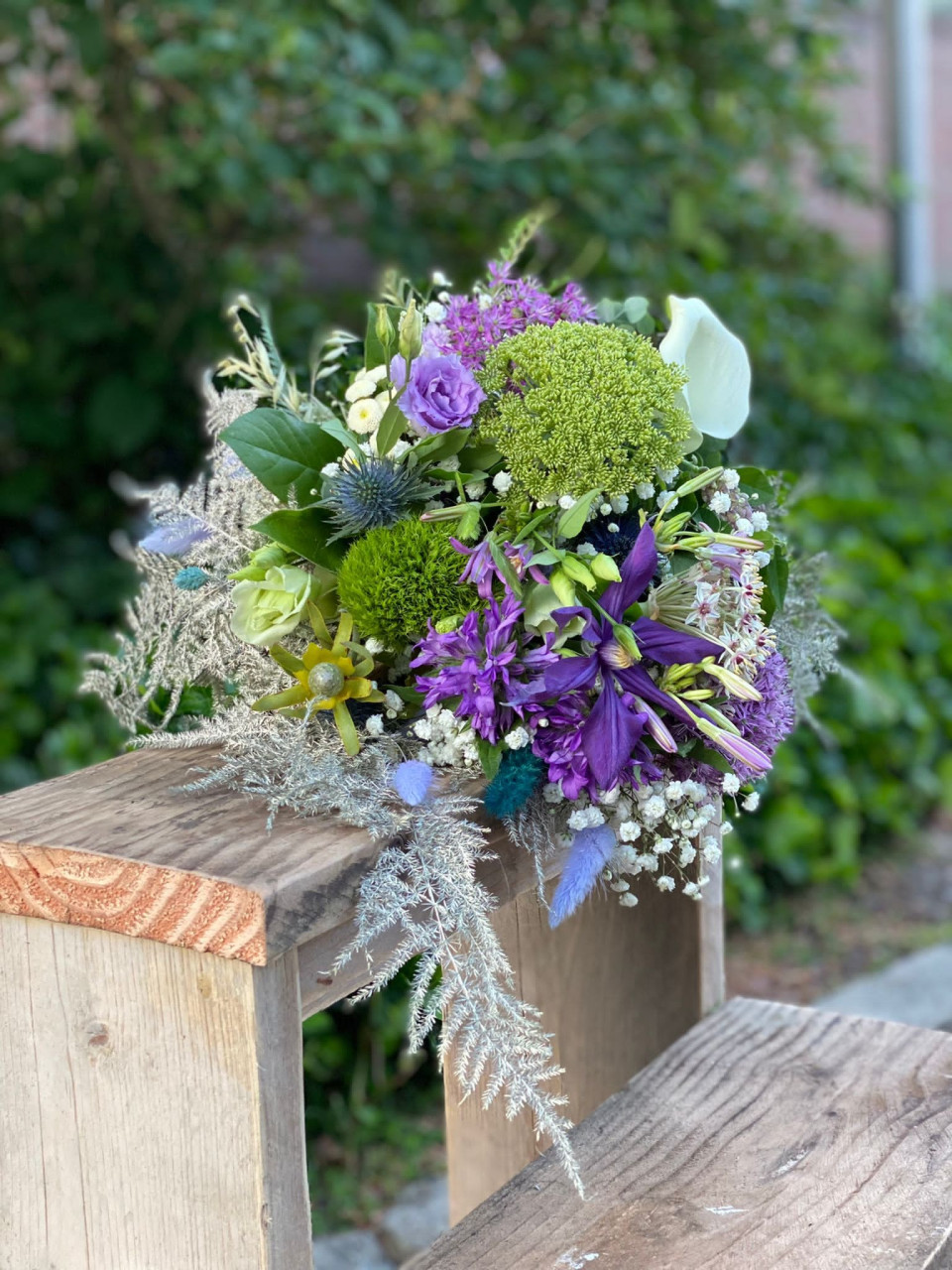 een boeket paarse en groene bloemen op een houten bank