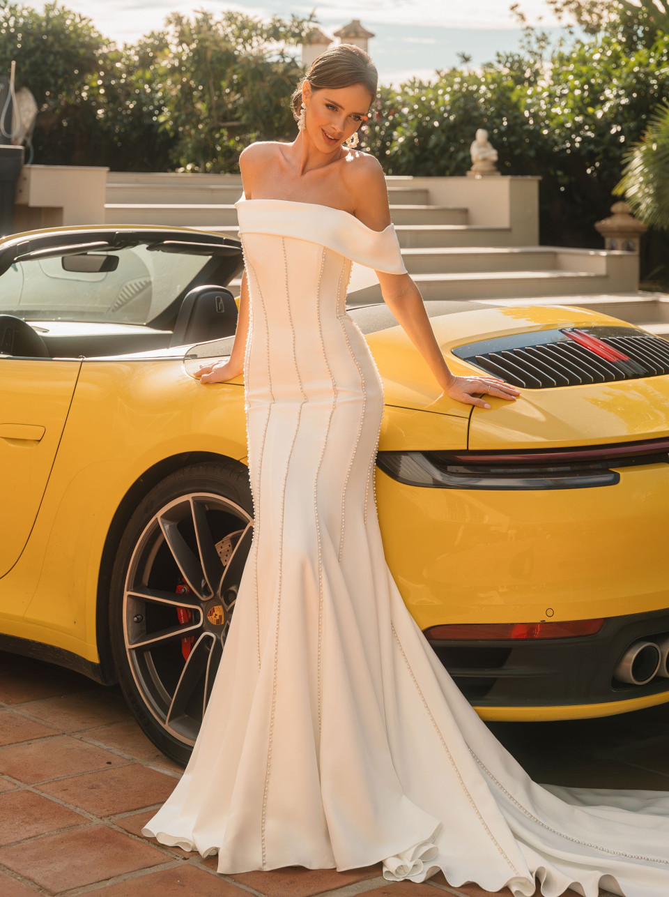 een vrouw in een witte jurk die naast een gele sportauto staat