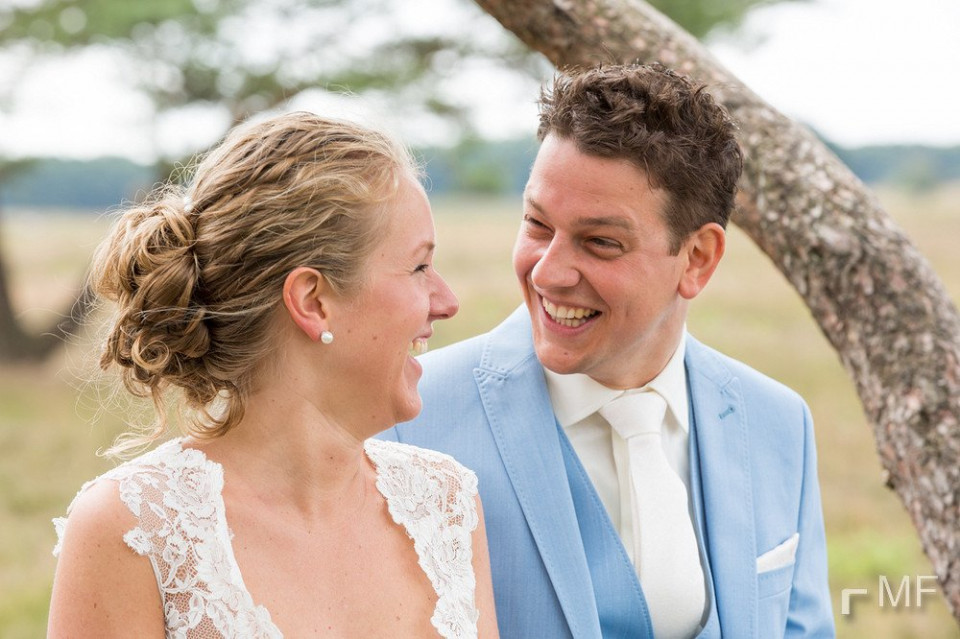 een bruid en bruidegom glimlachen terwijl ze voor een boom staan