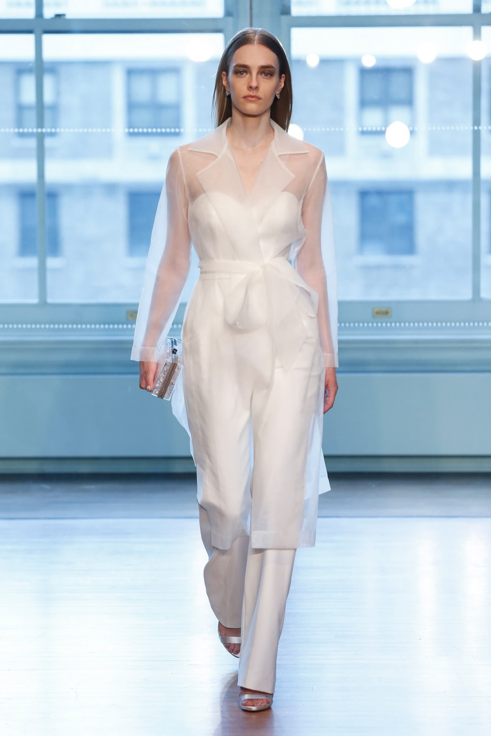 een model loopt op de catwalk in een wit jumpsuit