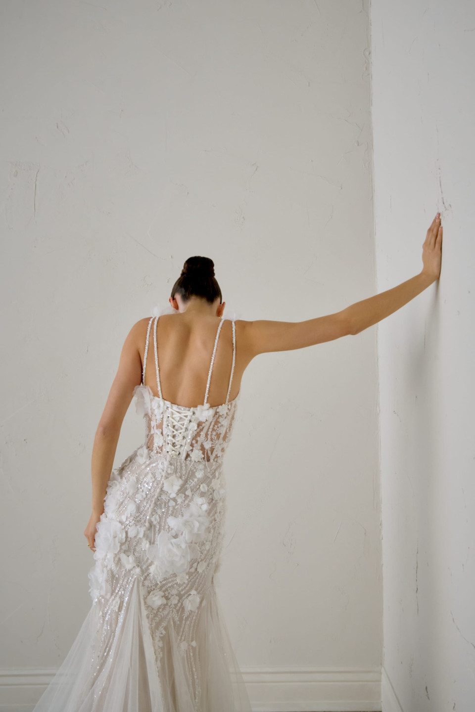 een vrouw in een trouwjurk leunend tegen een muur