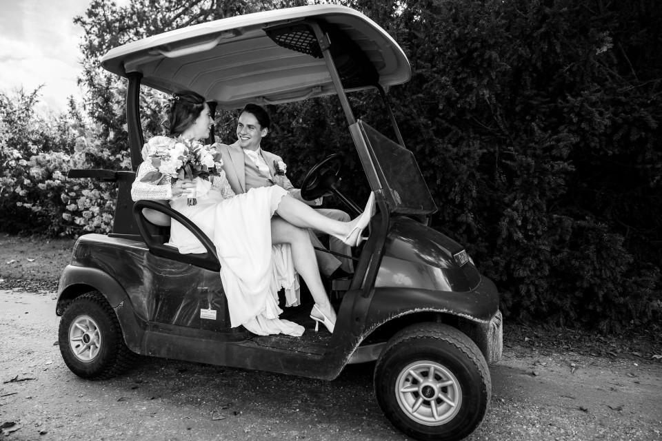 een zwart-wit foto van een bruid en bruidegom in een golfkar
