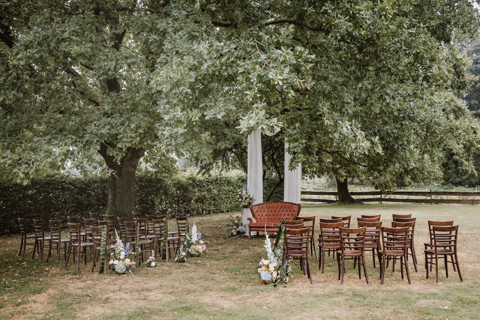 een paar rijen houten stoelen opgesteld onder een boom