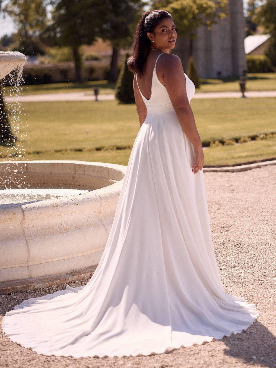 een vrouw in een witte jurk die voor een fontein staat