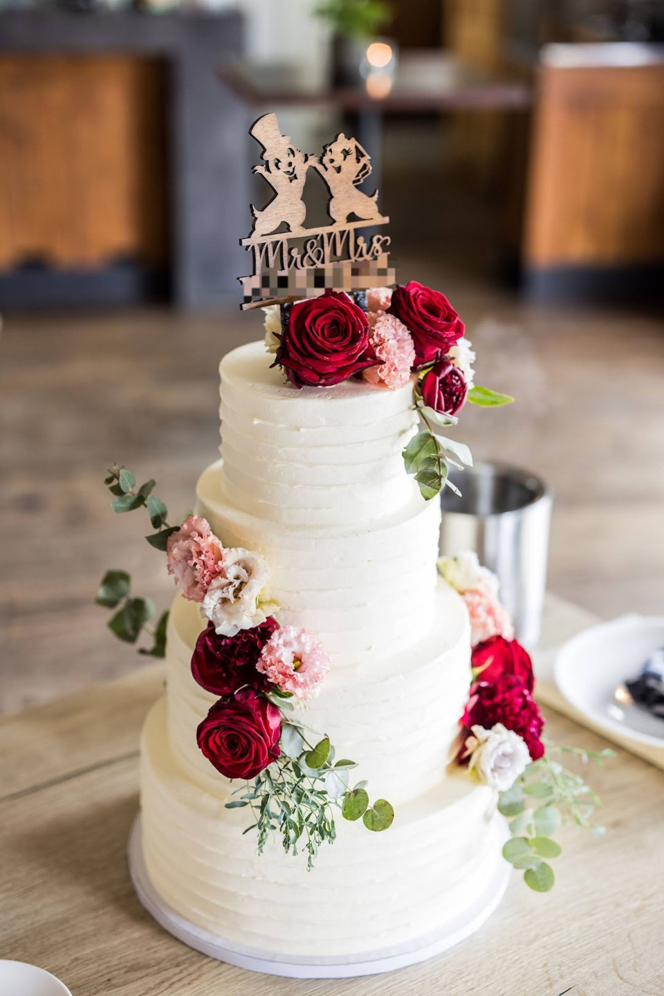 een close-up van een bruidstaart met rode bloemen op de bovenkant van de taart en een houten bord dat 'mr en mrs' zegt