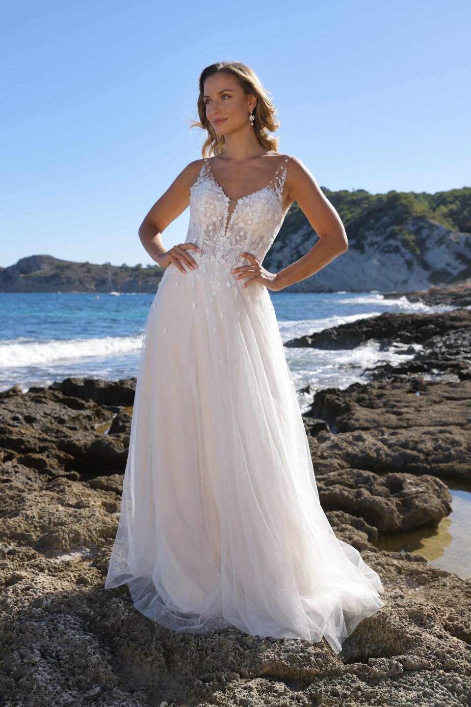 een vrouw in een trouwjurk die op een rotsachtig strand staat