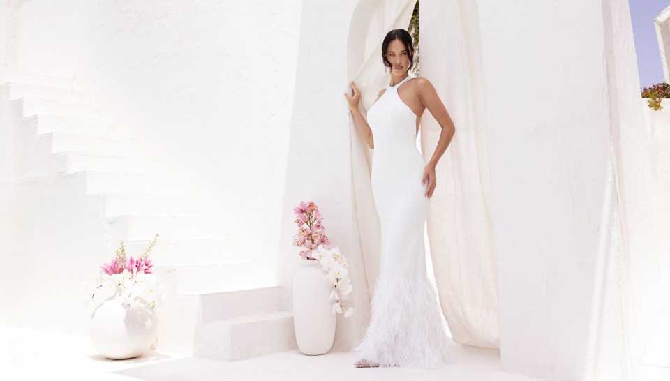 een vrouw in een witte jurk die voor een witte muur staat met bloemen in een vaas aan de zijkant van de trap