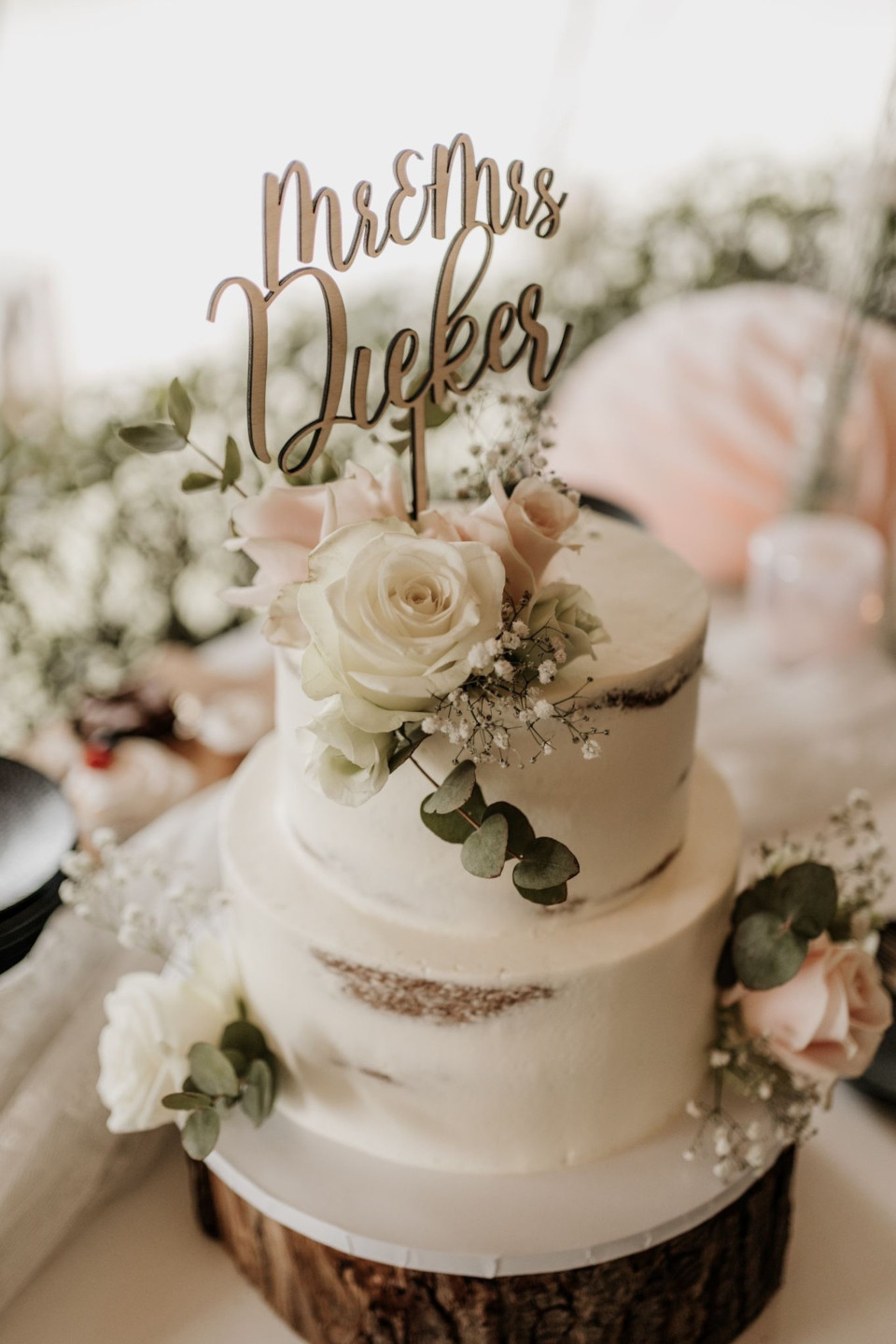 een close-up van een bruidstaart met bloemen en een taarttopper met het woord 'droom' erop geschreven