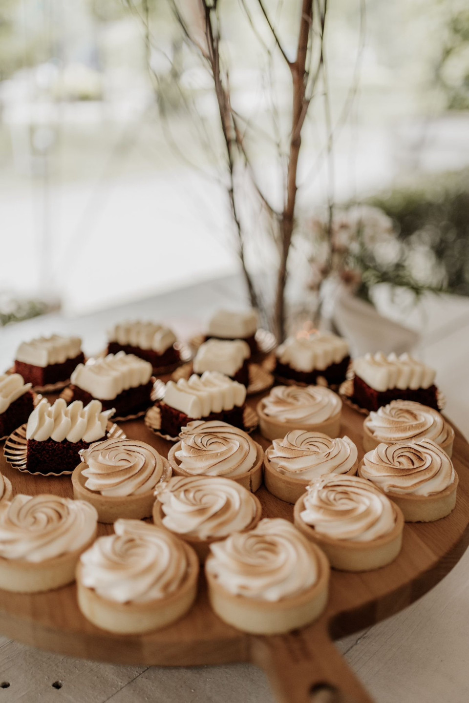 een schaal met cupcakes op een tafel met een boom op de achtergrond en een vaas met bloemen op de voorgrond