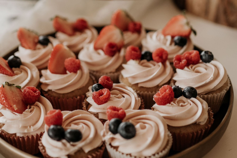 een bord met cupcakes met witte glazuur en aardbeien op elke cupcake