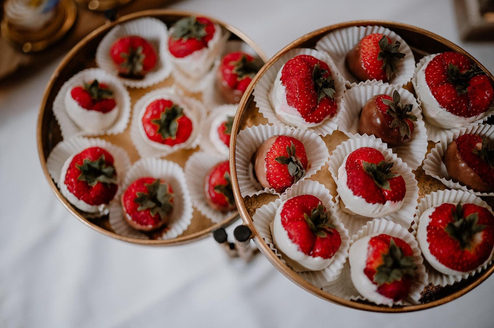 een paar manden met aardbeien die bovenop een bed van witte papieren muffins op een tafel liggen