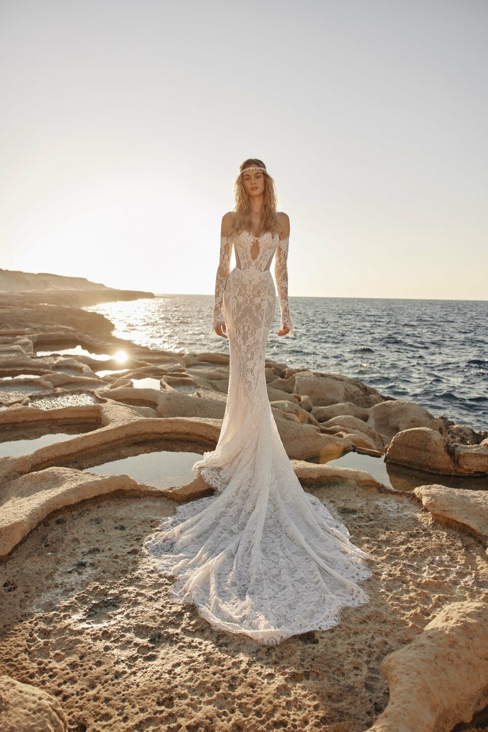 een vrouw in een trouwjurk die op een rots bij de oceaan staat