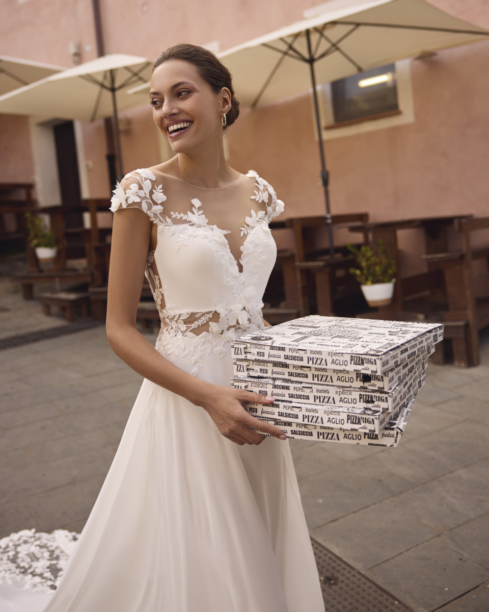 een vrouw in een trouwjurk die een doos pizza vasthoudt