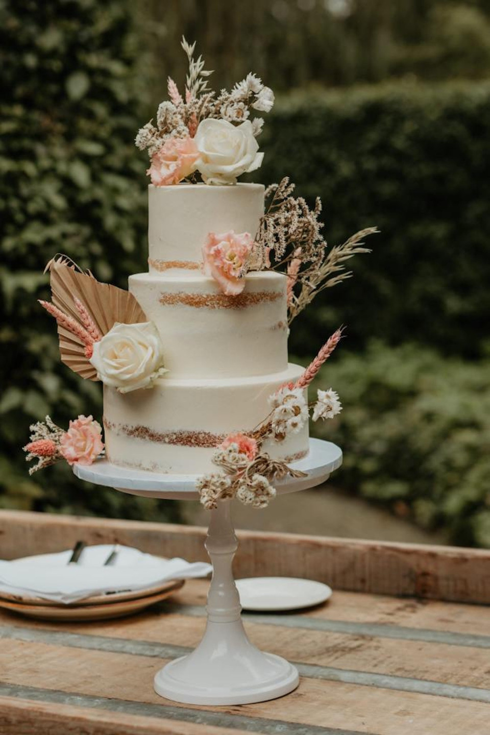 een witte taart met roze bloemen erop en een waaier aan de zijkant van de taart op een houten tafel