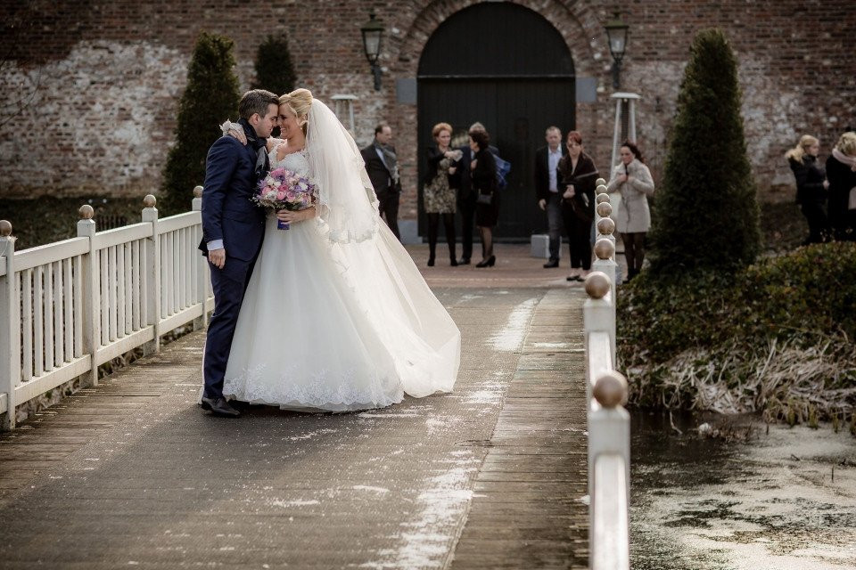 een bruid en bruidegom kussen op een brug voor een vijver