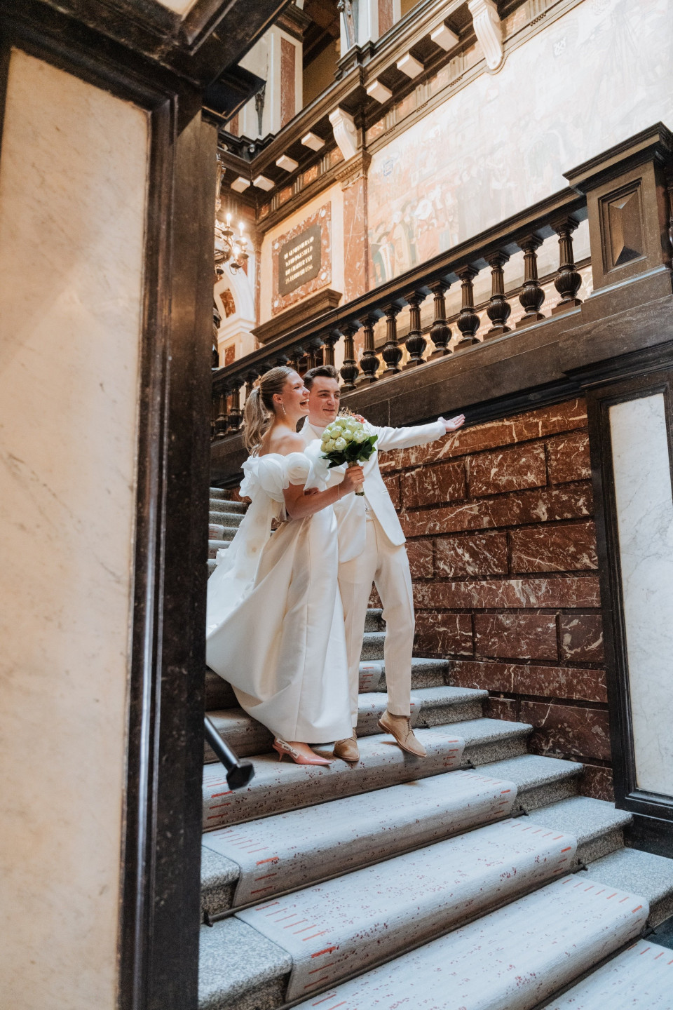 een afbeelding van een bruid en bruidegom die de trappen van een gebouw aflopen met hun handen in elkaars zakken