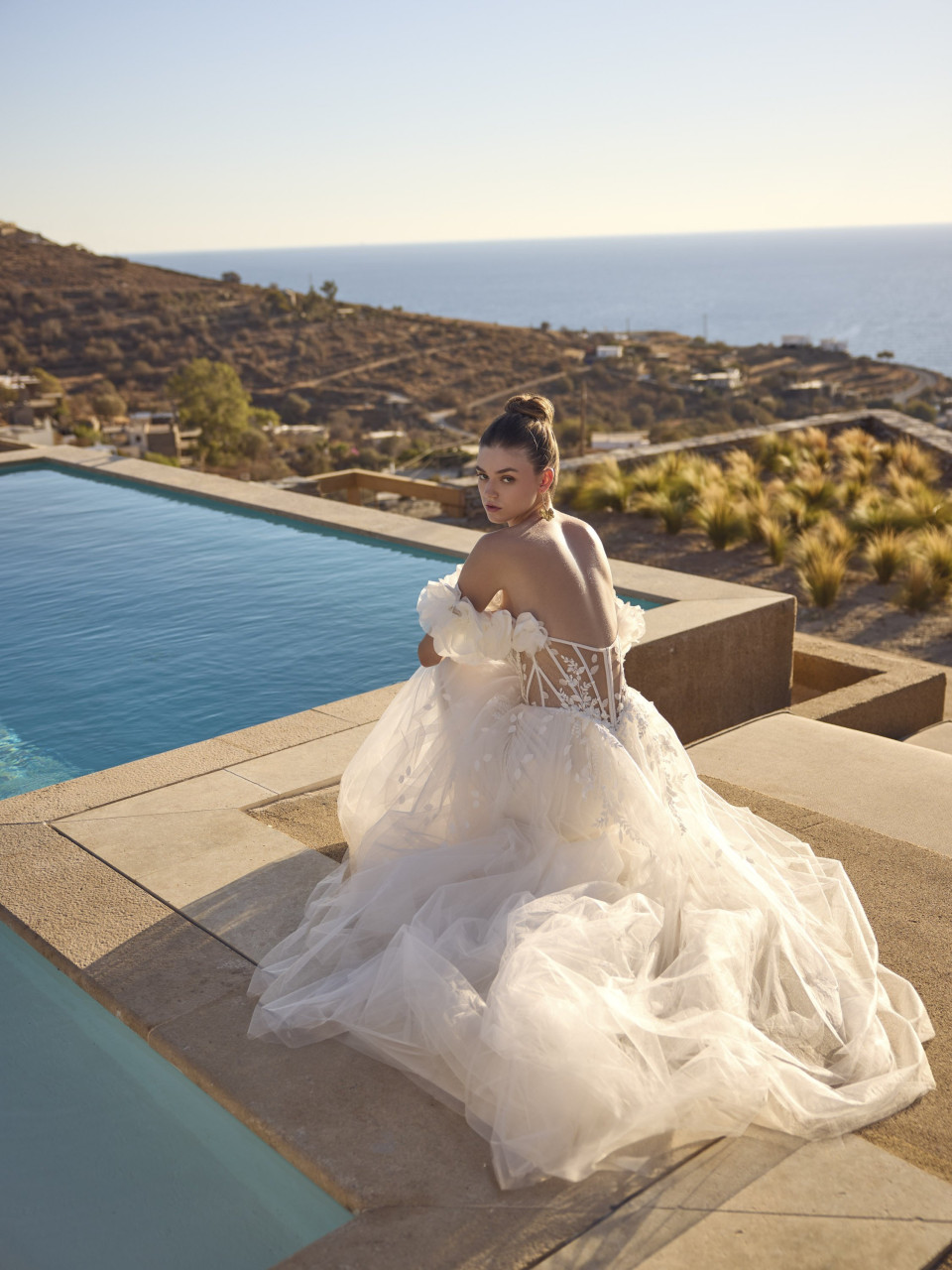 een vrouw in een trouwjurk die op de rand van een zwembad zit