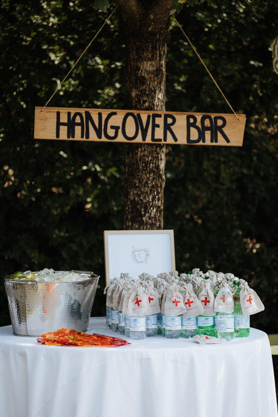 een bord dat zegt hangover bar naast een tafel met een emmer snoep en een bord dat aan een boom hangt