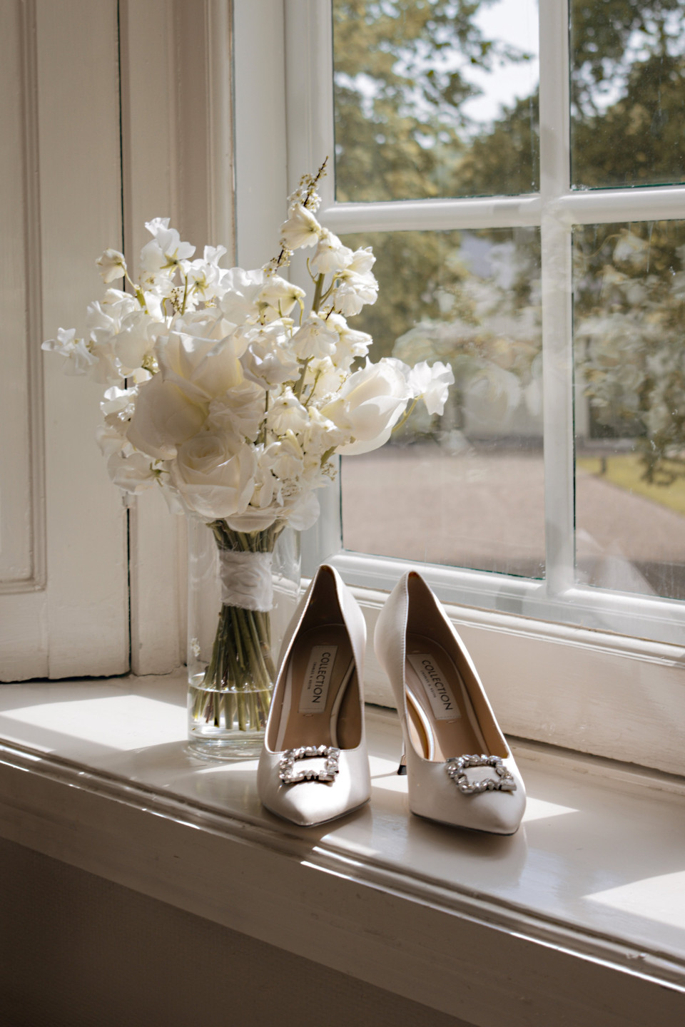 een vaas met witte bloemen en een paar schoenen op een vensterbank