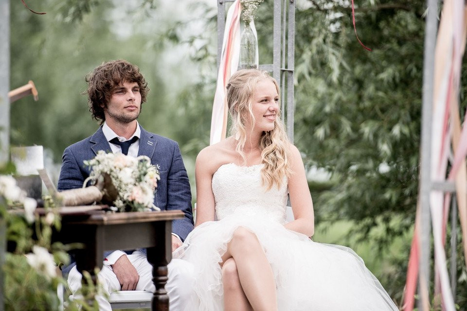 een bruid en bruidegom zitten op een bank voor een boom