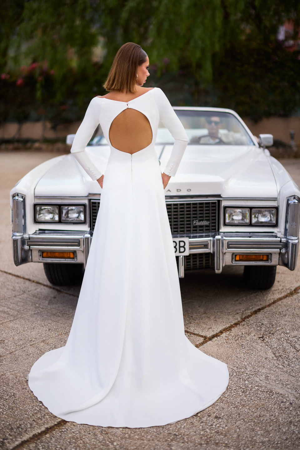 de achterkant van een vrouw in een witte jurk die voor een auto staat