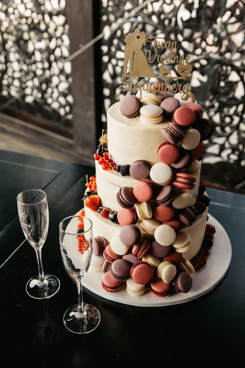 een afbeelding van een bruidstaart met macarons erop en een glas wijn aan de zijkant van de tafel
