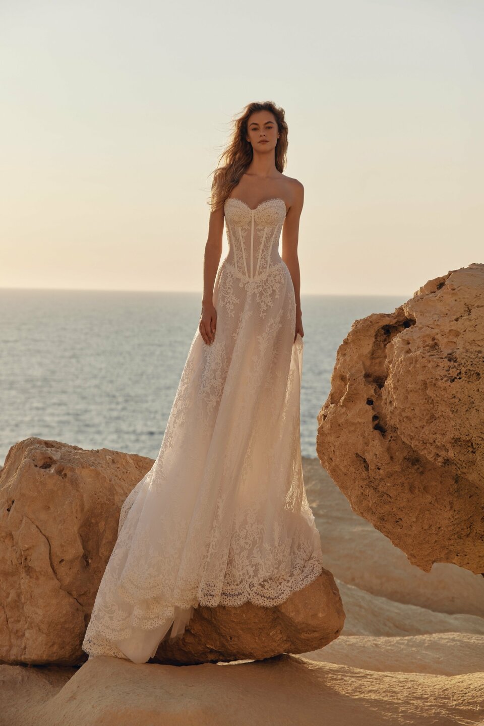 een vrouw in een trouwjurk die op een rots bij de oceaan staat