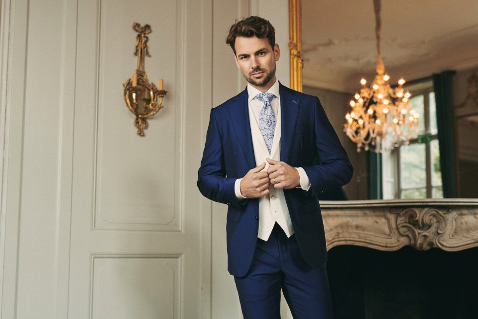 een man in een blauwe pak en stropdas staat voor een spiegel