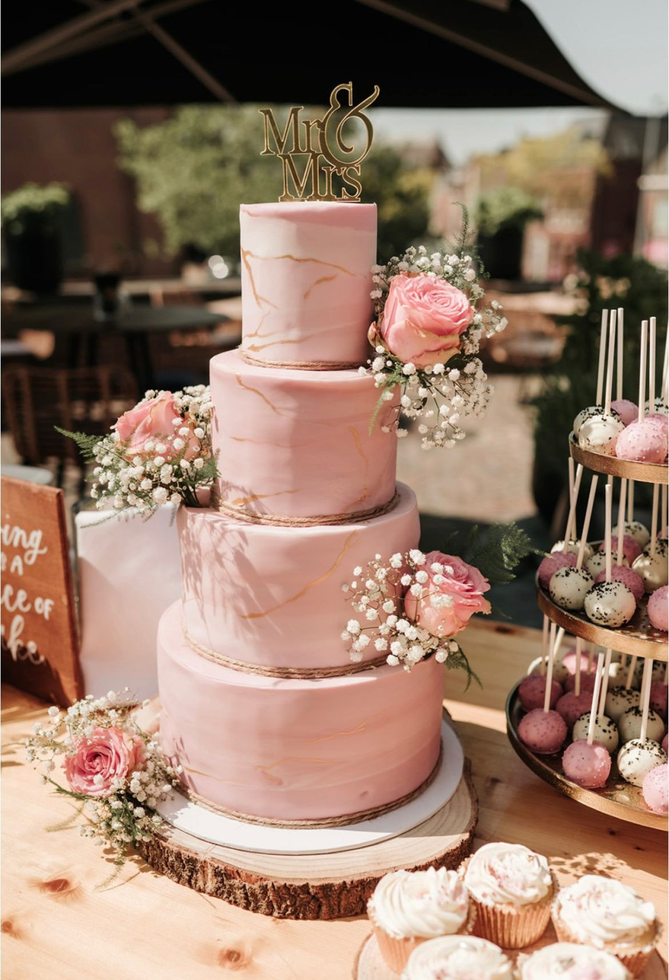 een roze bruidstaart en cupcakes op een tafel