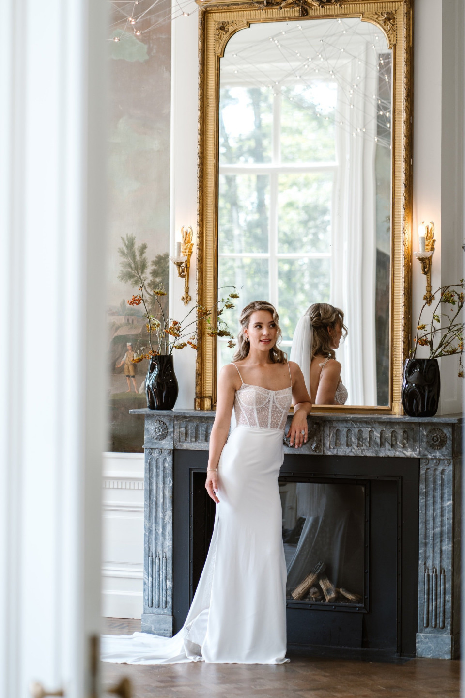 een bruid die poseert voor een spiegel in een kamer met een open haard
