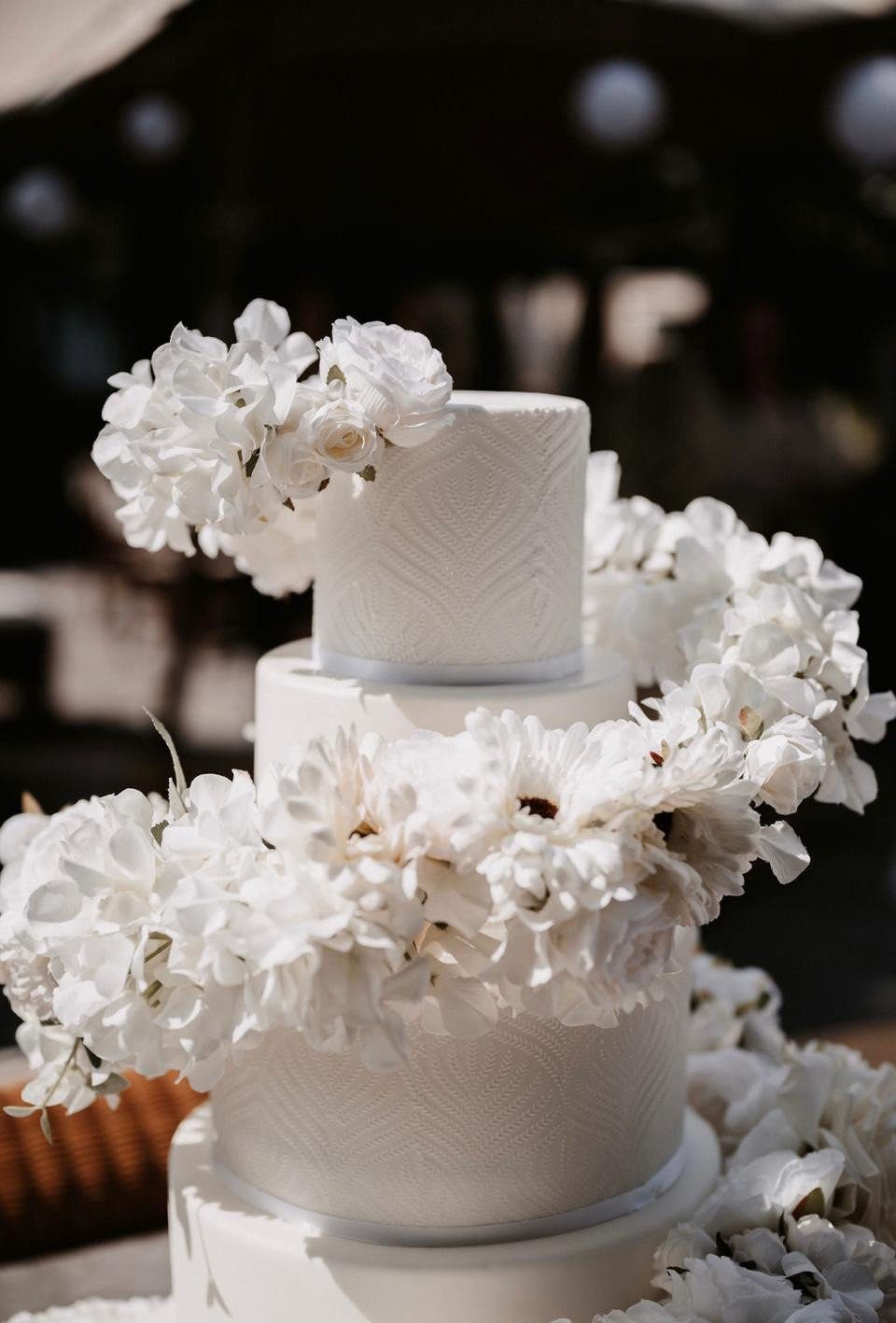 een witte bruidstaart met witte bloemen bovenop