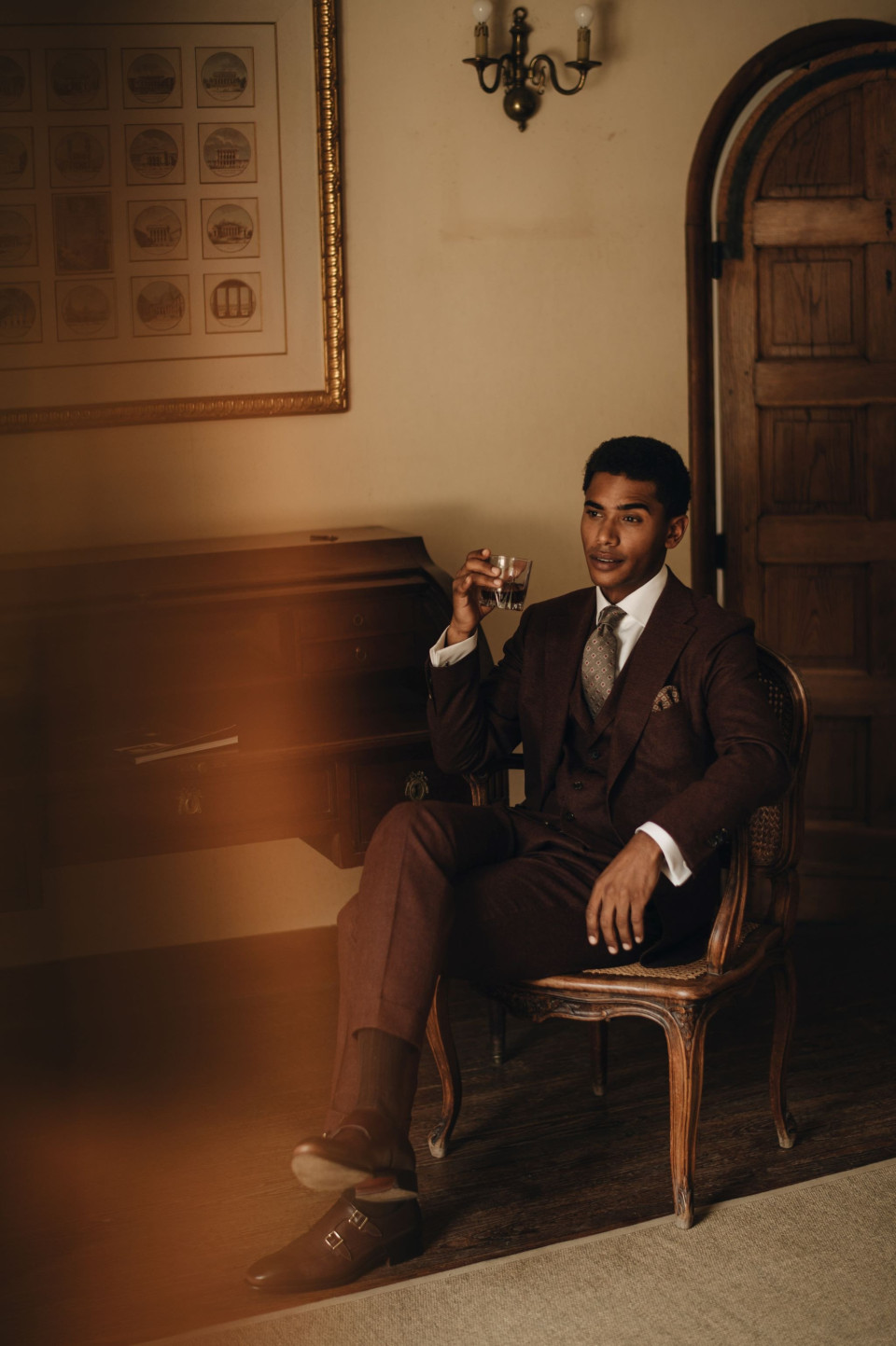 een man in een pak die op een stoel zit en een glas vasthoudt