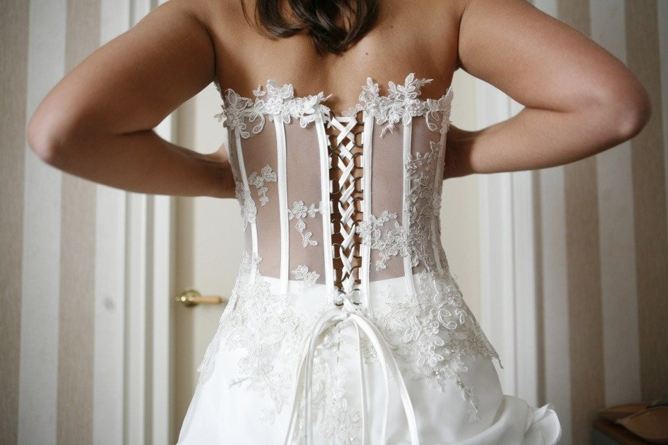 een vrouw in een trouwjurk die haar korset aanpast