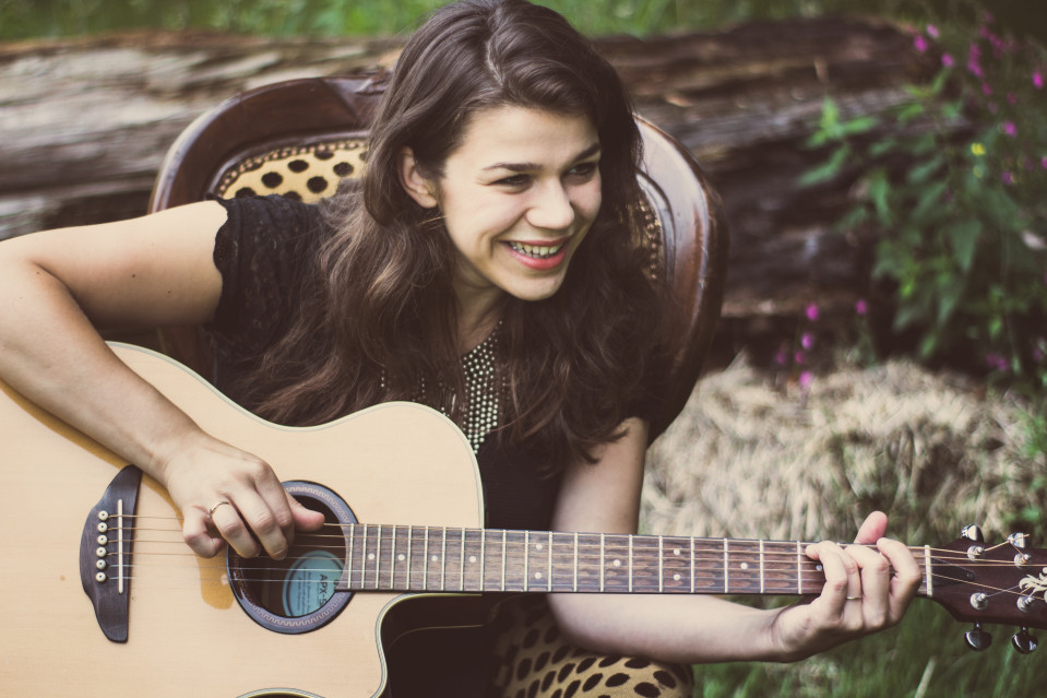 een vrouw glimlacht terwijl ze een akoestische gitaar vasthoudt