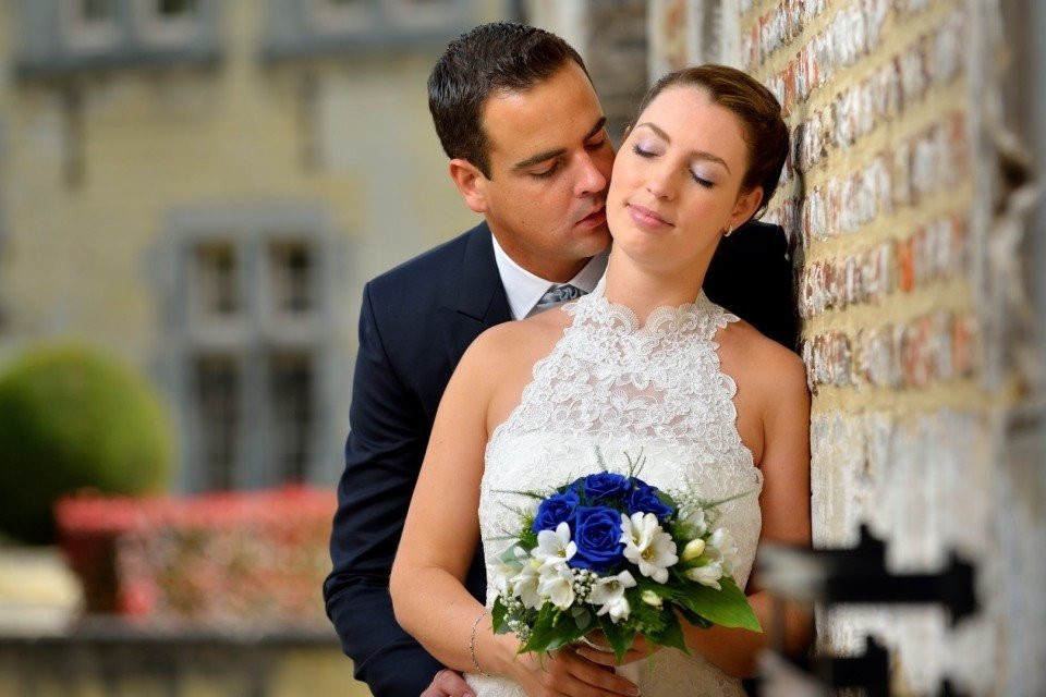 een bruid en bruidegom kussen voor een bakstenen muur