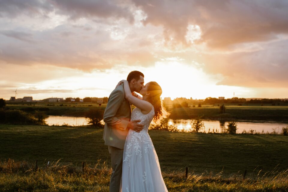 een bruid en bruidegom die elkaar kussen in een veld bij zonsondergang