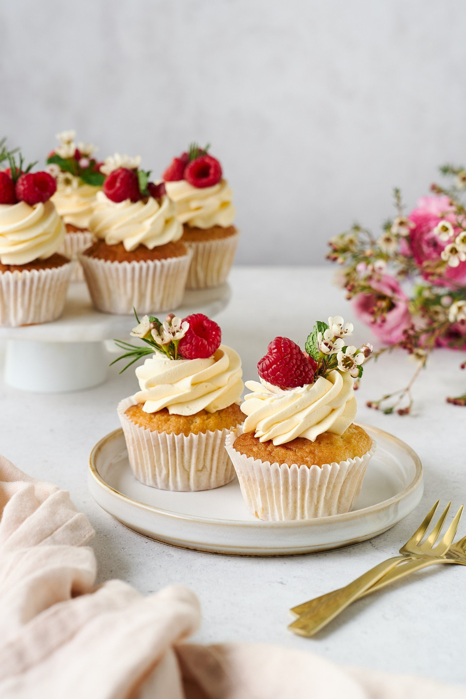 cupcakes met roomglazuur en frambozen op een wit bord