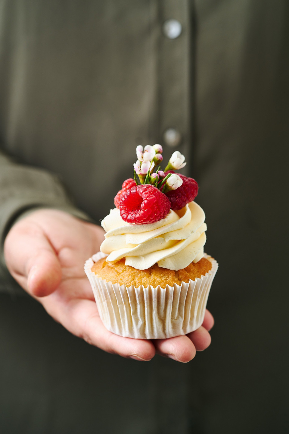 iemand die een cupcake met frambozen erop vasthoudt