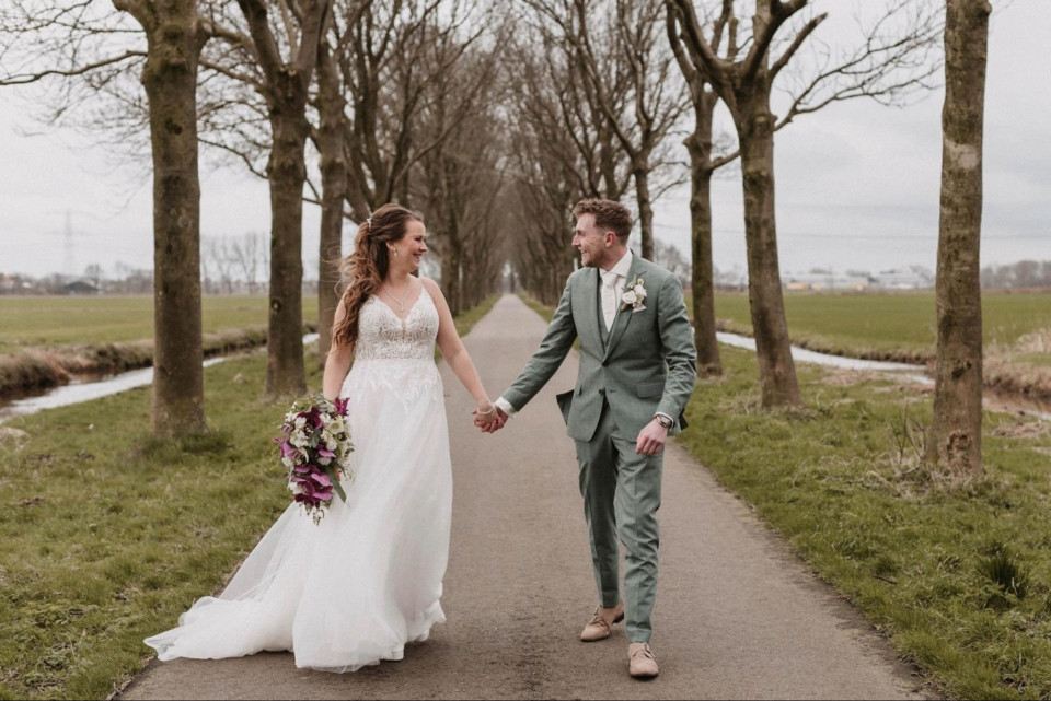 een bruid en bruidegom die hand in hand een pad aflopen