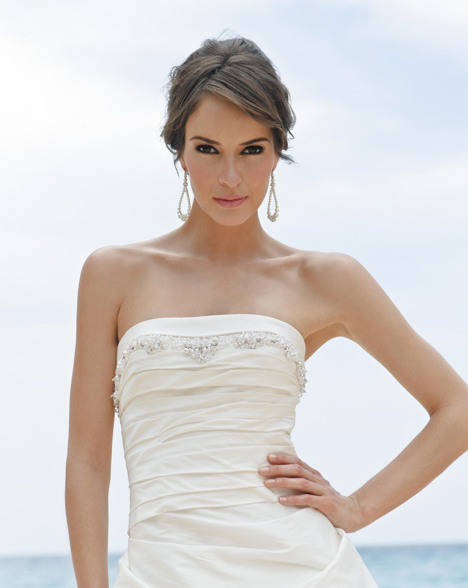 een vrouw in een strapless trouwjurk staat op het strand