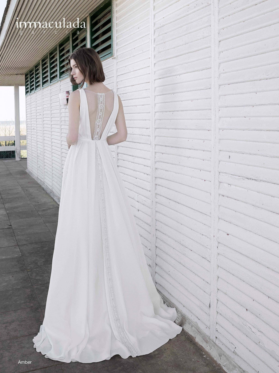 een vrouw in een witte trouwjurk die bij een muur staat