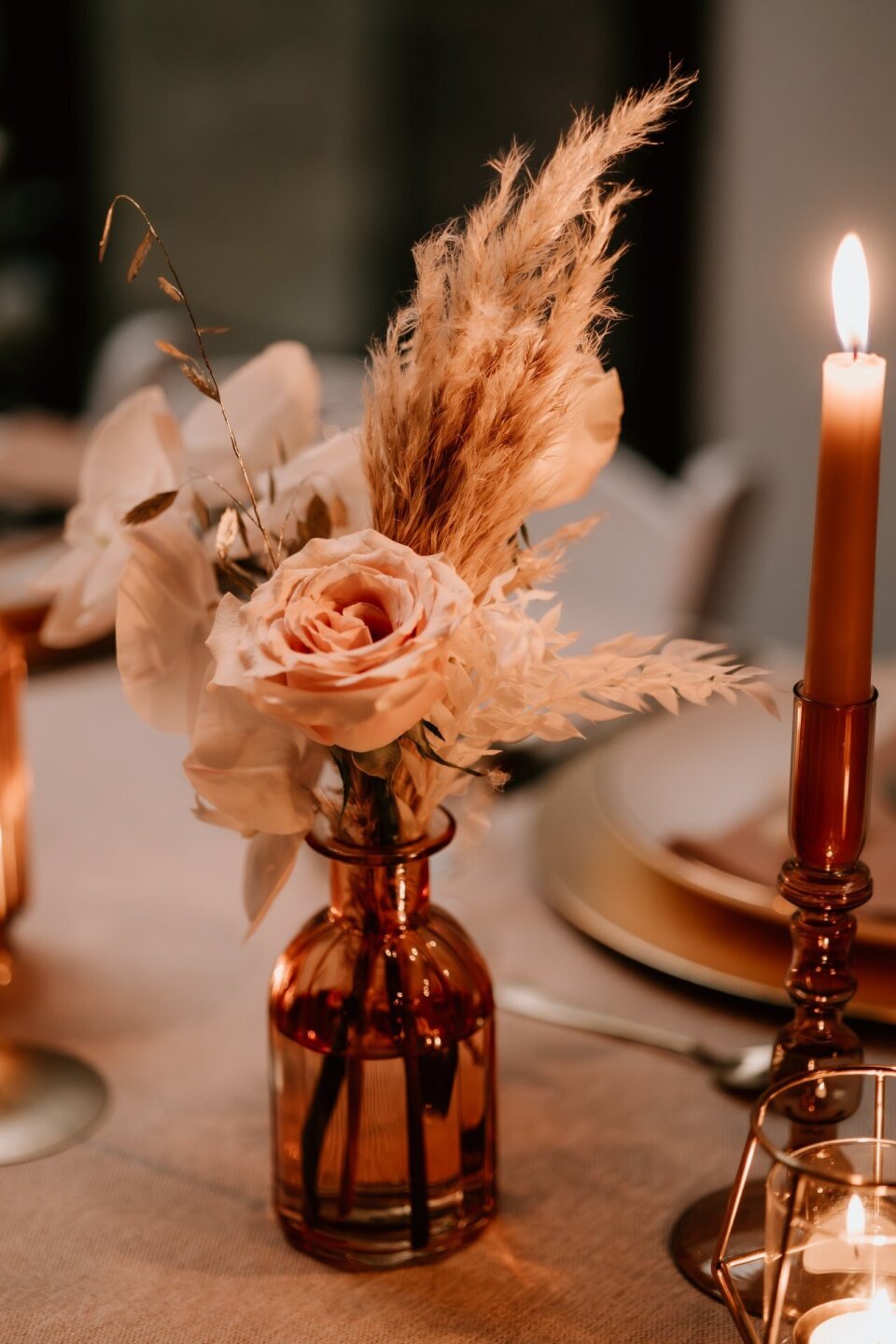 Amberkleurige vaasjes gevuld met bloemen en kaarsjes als tafeldecoratie