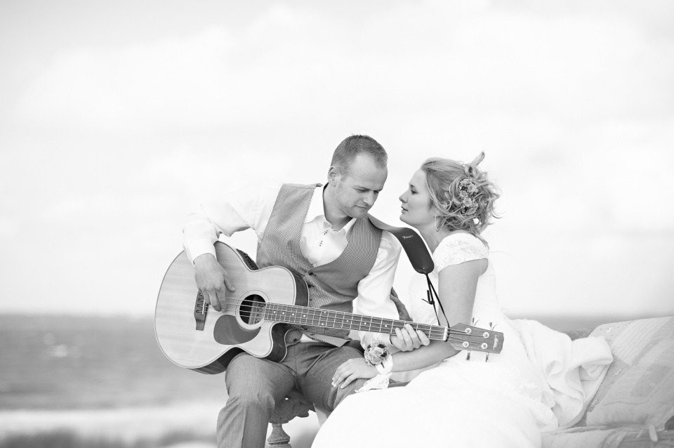 een bruid en bruidegom zitten op een bank met een gitaar