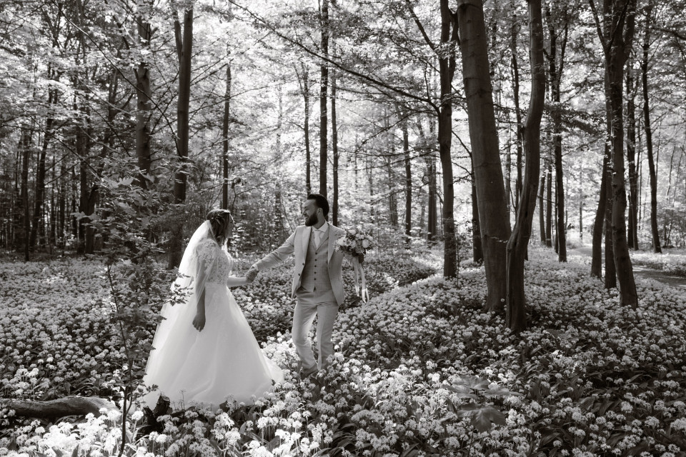 een zwart-wit foto van een bruid en bruidegom die door het bos lopen