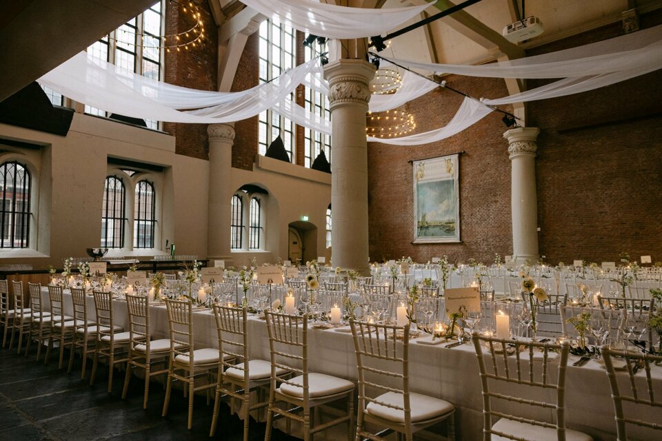 een lange tafel gedekt met witte tafellakens en kaarsen