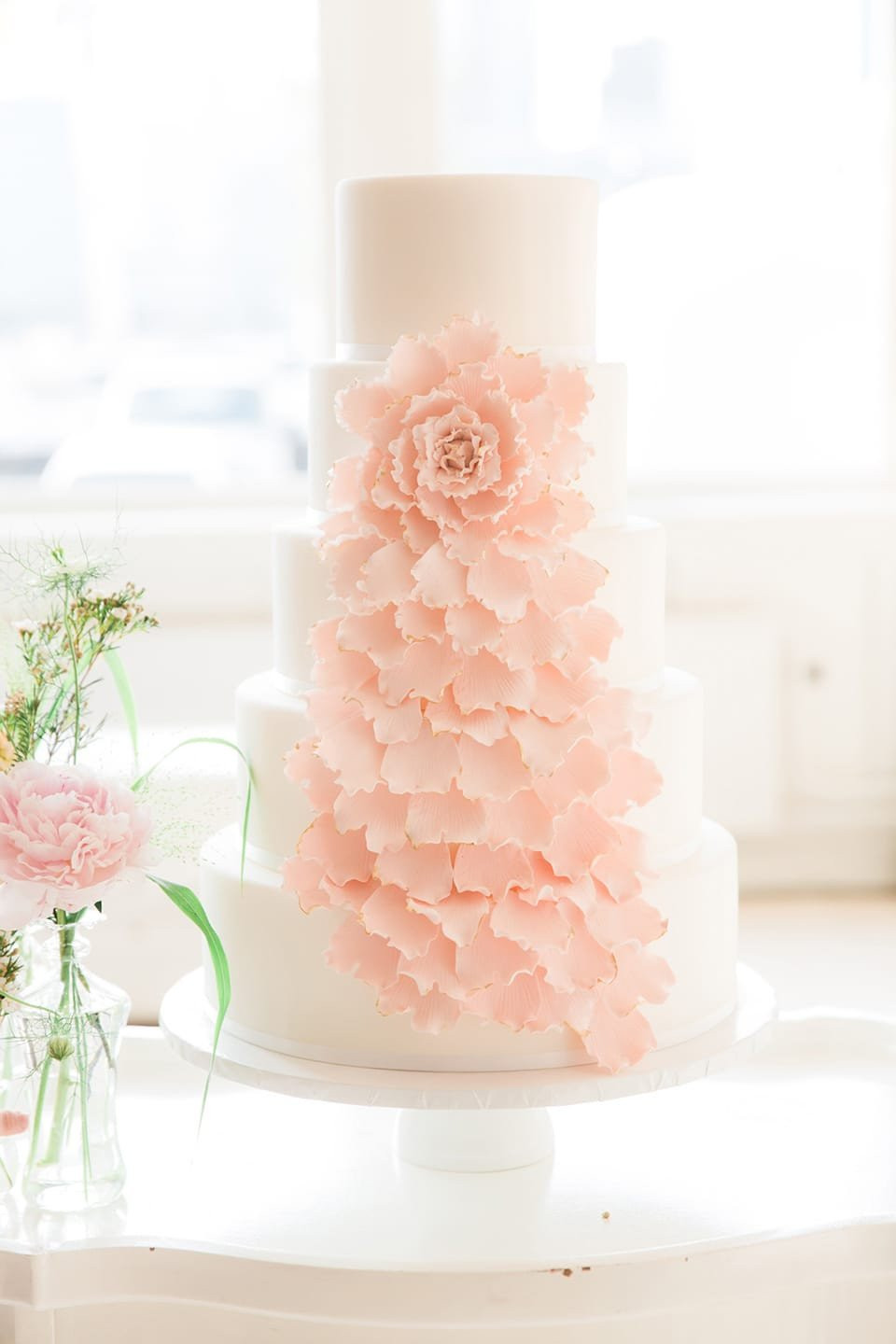 een bruiloftstaart met roze bloemen erop