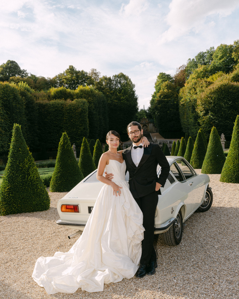 een bruid en bruidegom die voor een auto staan