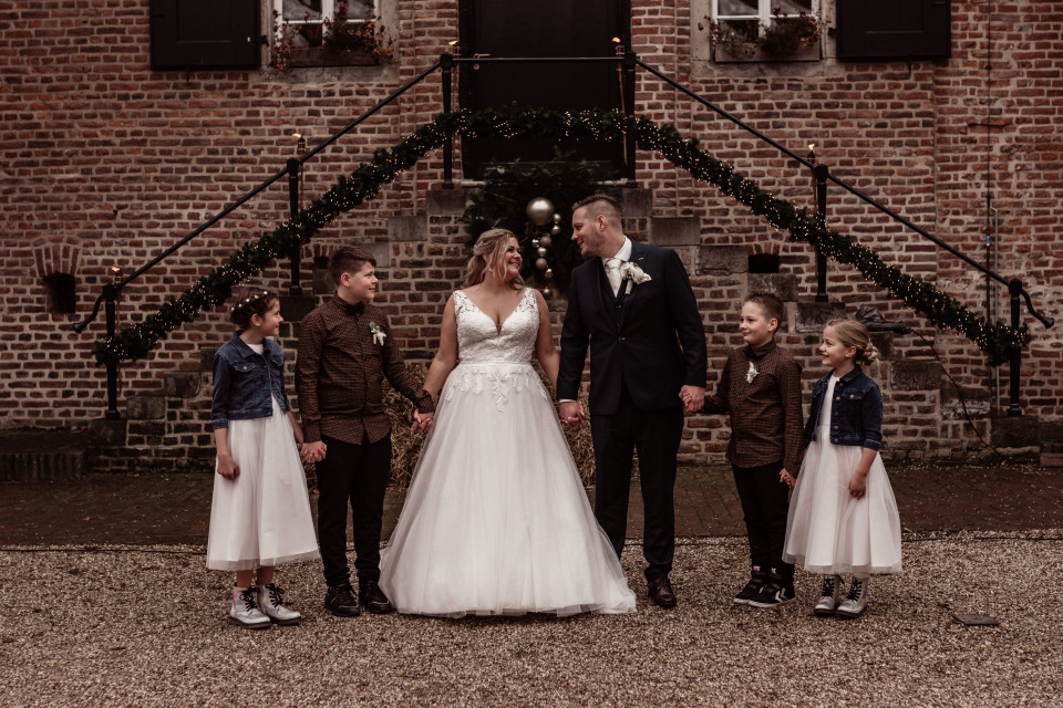 een bruid en bruidegom met hun kinderen voor een bakstenen gebouw
