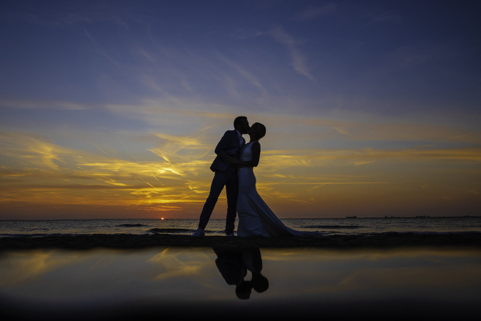een bruid en bruidegom kussen bij zonsondergang op het strand