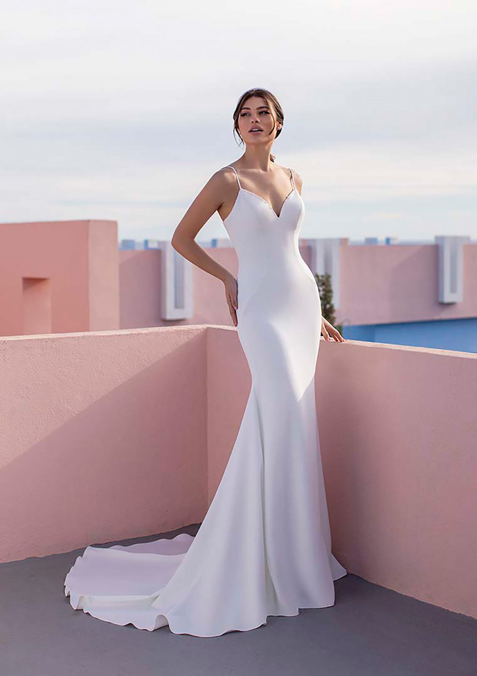 een vrouw in een witte trouwjurk staat op een roze muur